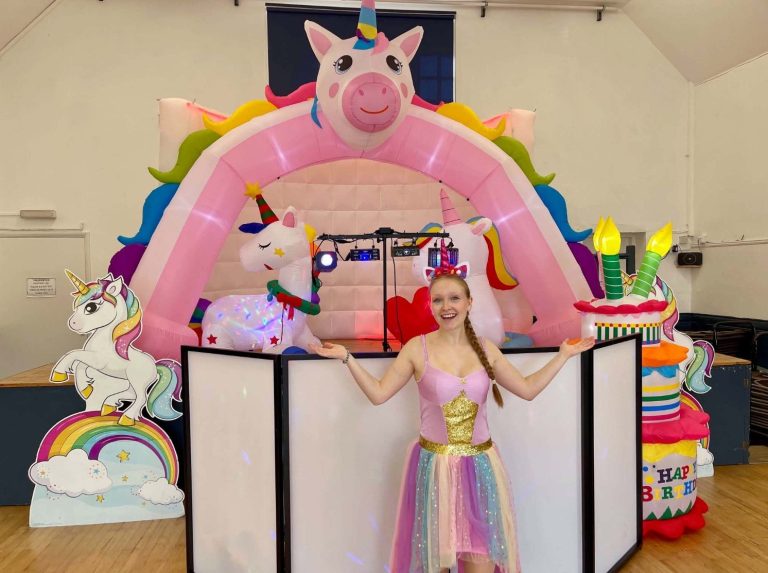 Unicorn entertainer at a rainbow pig and unicorn themed DJ booth with cake inflatables