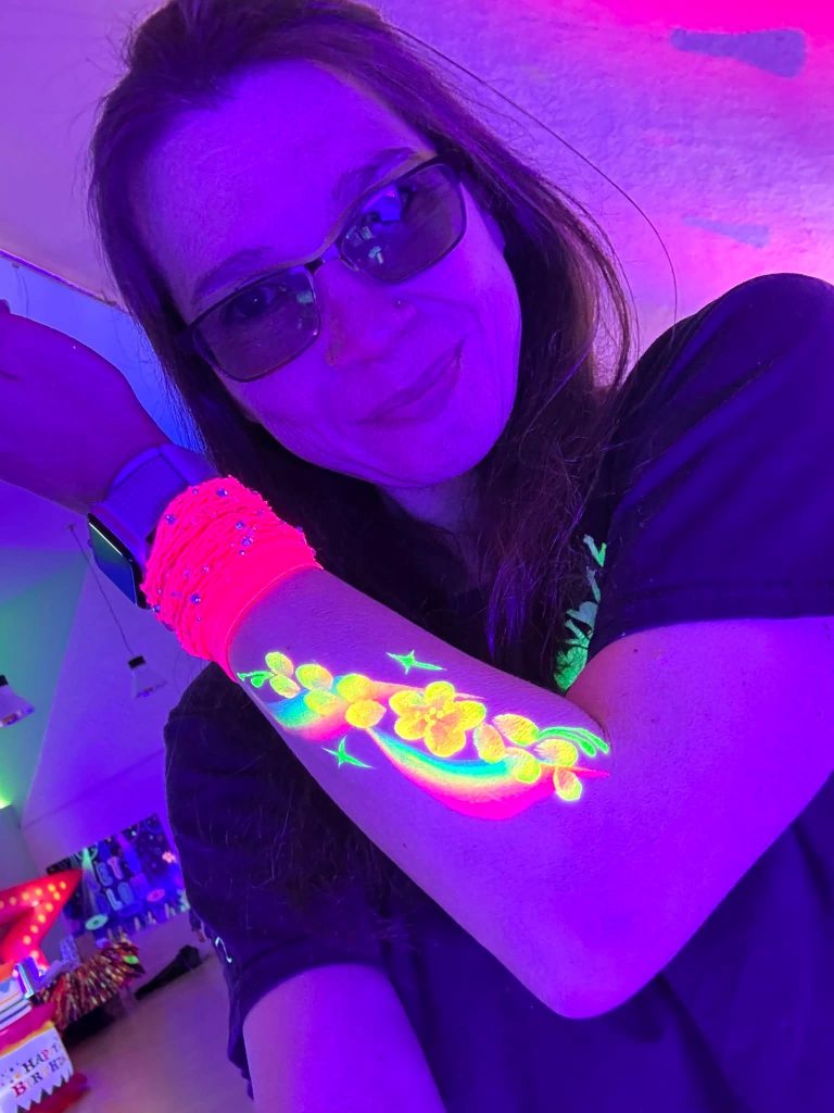 Glowing UV body paint flowers on an arm under black light