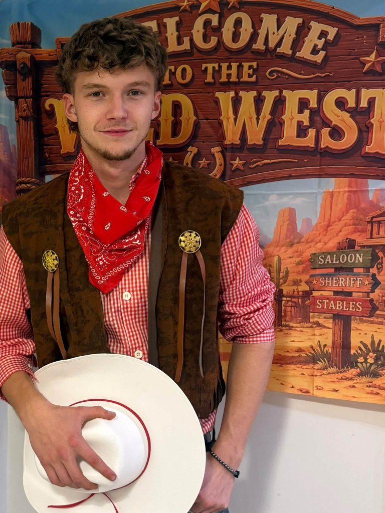 Cowboy entertainer holding a hat in front of a Welcome to the Wild West backdrop